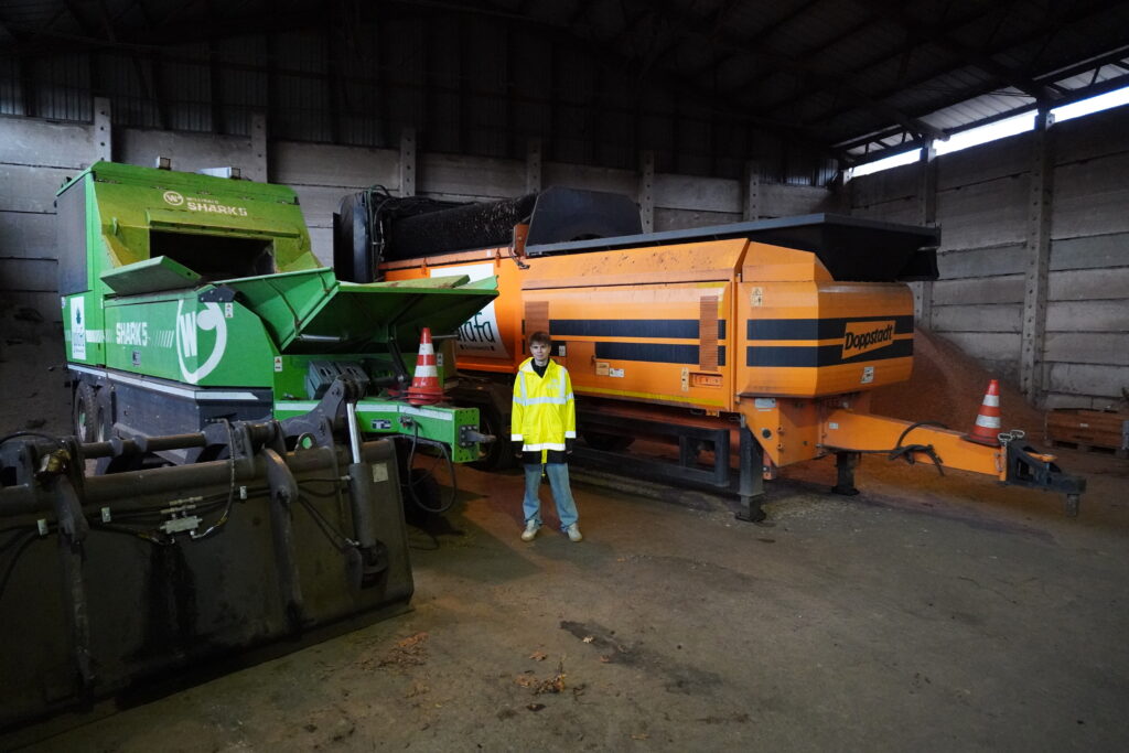 Mitarbeiter in reflektierender Jacke steht zwischen zwei Maschinen, einer grünen "Shark 5" und einer orangefarbenen "Dopstart".